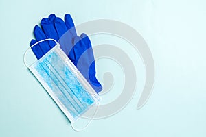 Top view of disposable medical mask and nitrile gloves on blue background. Personal protection concept with copy space