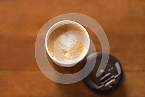 Top view of disposable take away paper cup of hot coffee latte with heart shape art milk foam with lid cover on wooden table