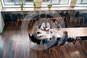 Top view of a diverse group of professionals in a meeting. A female CEO leads a business consultation at a modern office