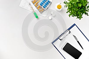 Top view of doctor`s desk table, blank paper on clipboard with pen, electronic thermometer and tablets in capsules. Copy