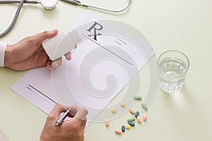 Top view of a doctor`s hand writing a prescription. A pill bottl