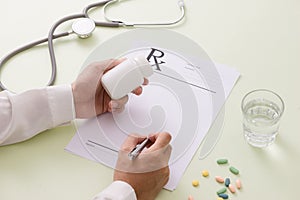 Top view of a doctor`s hand writing a prescription. A pill bottl