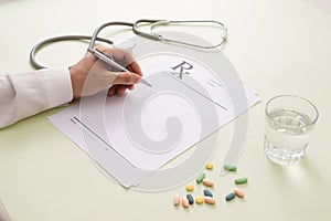Top view of a doctor`s hand writing a prescription. A pill bottl