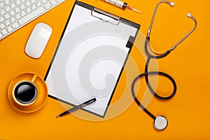 Top view of a doctor`s table with notepad and pen stethoscope, keyboard, prescription and pills, a cup of coffee on a yellow