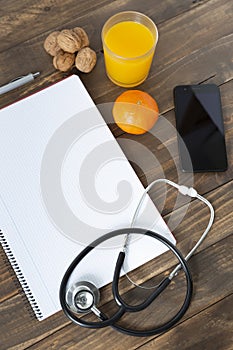 Top view of a doctor`s work desk. Notebook, stethoscope and mobile phone on wood background