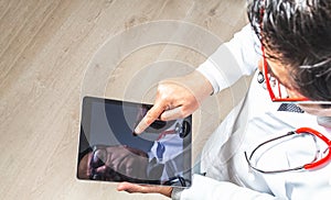 Top view of a doctor in a white coat, tie and stethoscope working on his tablet