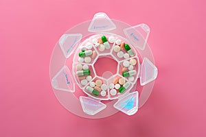 Top view daily doses pills in a plastic container on pink photo