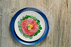 Top view of double plated beef steak tartare served with three raw quail egg yolks and surrounded by watercress leaves on a
