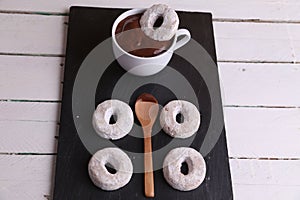 Top view of doughnuts a cup of hot chocolate with a doughnut dipping in and a wooden spoon