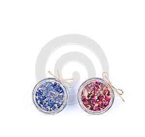 Dried blue cornflower centaurea petals and red rose petals in a glass jars isolated on white background