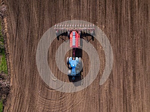 Top view from drone of big tractor with cultivator ploughs field
