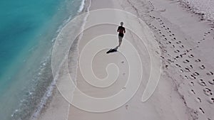 Top view from the drone on fit man run along ocean surf by water to keep fit and health. Man fitness, jogging training