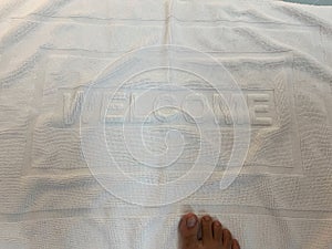 Top view of dry feet on white cotton welcome mat in the bathroom