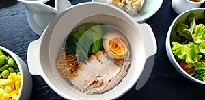 Top view of dry noodle with boiled belly pork, egg and garlic on white bowl with fresh salad, green cabbage, corn and bean.