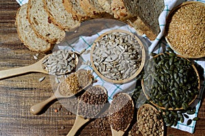 Top view of dry organic sunflower seeds in wooden bowl over blur whole wheat bread, golden flax and pumpkin seed