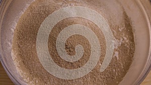 Top view of dry yeast falls into a glass bowl of flour. Mixing ingredients for kneading dough. Food blog, flour and