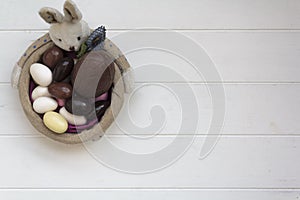 Top view of Easter Bunny basket with chocolate almond eggs on white wooden table with copy space