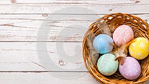 Top view of easter eggs hand painted in pastel colors and tender feathers in a wicker basket on wooden table