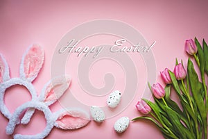 Top view of Easter eggs, pink tulips and two white fluffy bunny ears over pink background. Easter concept background. Happy Easter
