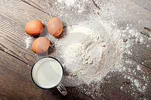 Top view of the egg, flour, a glass of fresh milk, cooking dough on the background of a wooden table. Flat lay