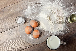 Top view of the egg, flour, a glass of fresh milk, cooking dough on the background of a wooden table. Flat lay, copy space