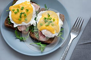 Top view on eggs Benedict with arugula, bacon and hollandaise sauce on gray wooden background. Soft focus. Healthy eating concept