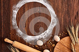 Top view eggs, dough, flour and rolling-pin on wooden table