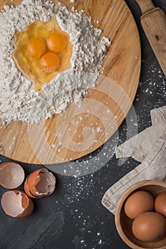 Top view eggs, dough, flour and rolling-pin on wooden table back