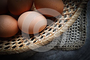 Top view of eggs in a straw basket on a natural linen napkins and a rustic wooden background