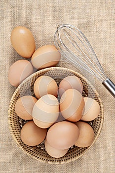 Top view of eggs in a wooden basket and egg whisk