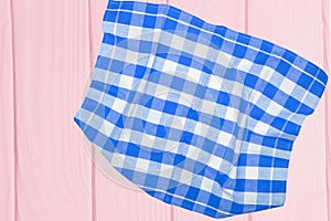 Top view of a empty blue and white checkered kitchen cloth, textile, tablecloth or napkin on blurred light pink wooden background