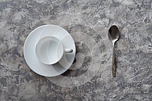 Top view of empty cup on saucer and spoon on gray background