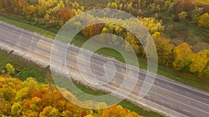 Top view of empty highway surrounded by bright autumn forest.