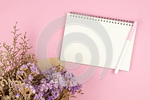 Top view of empty notebook and flower bouquet on pastel pink background