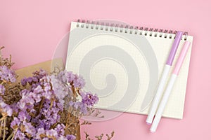 Top view of empty notebook and flower bouquet on pastel pink background