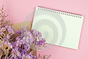 Top view of empty notebook and flower bouquet on pastel pink background