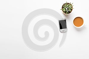 Top view of empty office desk. Green plant in a pot, cup of coffee and pocket communicator smart phone on white background. Copy