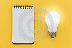 Top view of empty open blank notebook and LED light bulb on yellow background with copy space,  ideas concept, flat lay