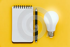 Top view of empty open blank notebook, pen and LED light bulb on yellow background with copy space, ideas concept, flat lay