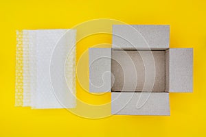 Top view of empty open brown paper cardboard box and translucent white plastic bubble wrap  on yellow background