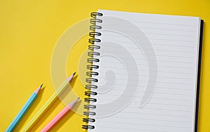 Top view of empty open lined notebook with pastel color pencils on yellow background with copy space, flat lay