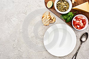 Top view of empty plate near wooden cutting board with fresh ingredients.