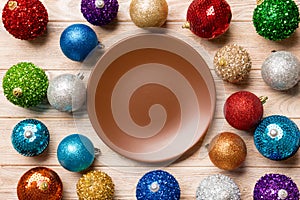 Top view of empty plate surrounded with colorful baubles on wooden background. New Year decorations. Christmas Eve concept