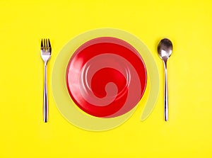 Top view of empty red dish with spoon and fork on vibrant yello