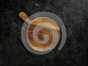 Top view of empty round wooden cutting board with handle on beautiful dark background