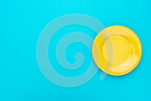 Top view of empty round yellow plate on turquoise blue background with copy space