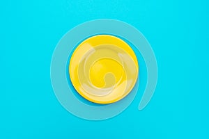 Top view of empty round yellow plate on turquoise blue background with copy space