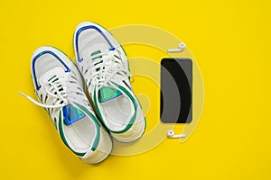 Top view of empty white sneakers with blue and green decorations on the edgings, black mobile phone and white wireless earphones