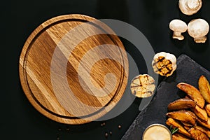 top view of empty wooden board, grilled garlic, mushrooms and baked potatoes with sauce