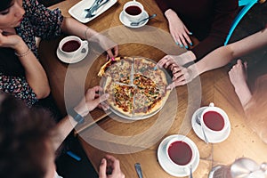 Top view of family members having lunch reaching out for pizza pieces in pizzeria